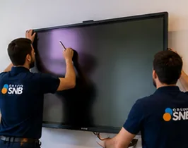 Dos técnicos de Grupo SNB instalando una pantalla en la pared.